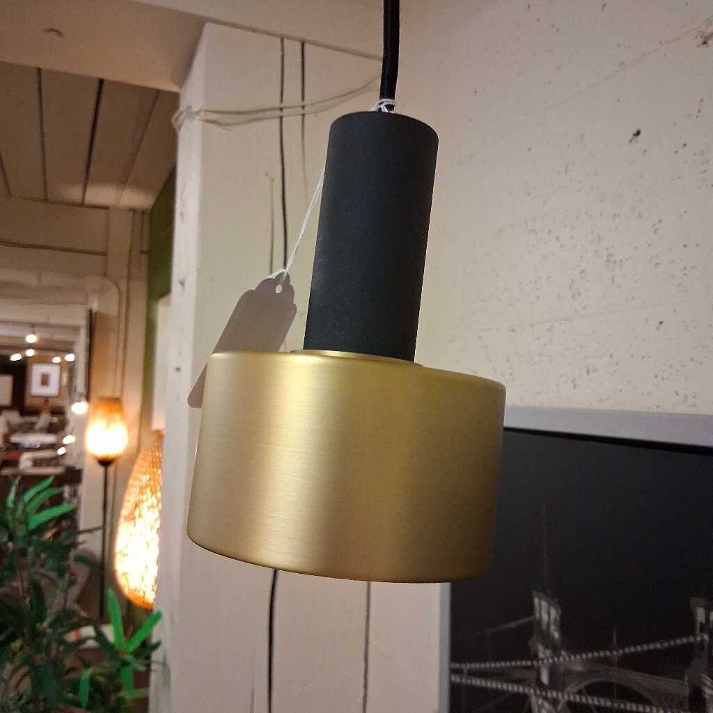 Gold pendant light with black shade hanging in a room with plants and furniture.