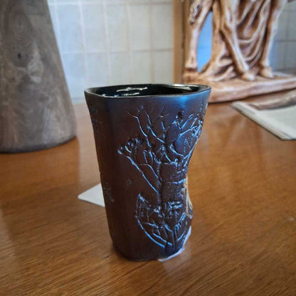 Dark brown ceramic cup with embossed design on a wooden surface