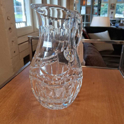 Clear glass pitcher on a wooden table with a blurred indoor background