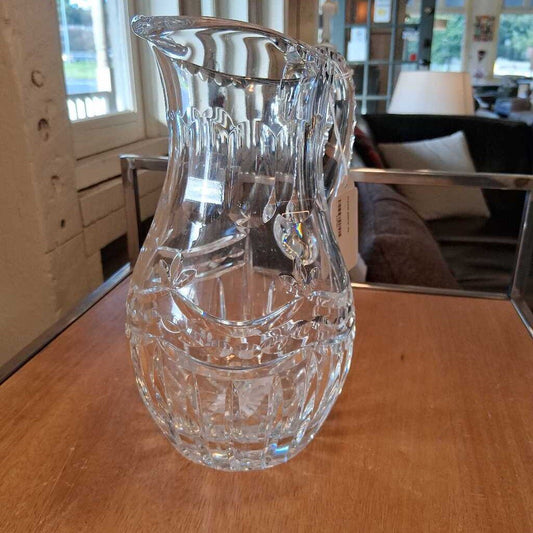 Clear glass pitcher on a wooden table with a blurred indoor background