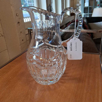 Clear glass pitcher with a tag on a wooden surface