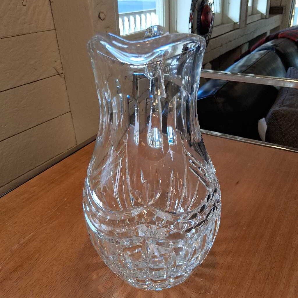 Clear glass pitcher on a wooden surface with a blurred background