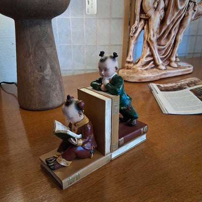 Two figurines on books on a wooden surface with a statue in the background.