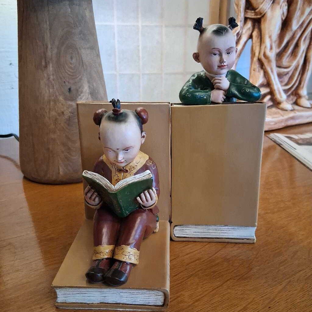 Two figurines of children reading books on a wooden surface.