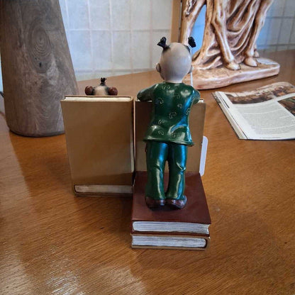 Small figurine of a child in a green outfit standing on books on a wooden surface.