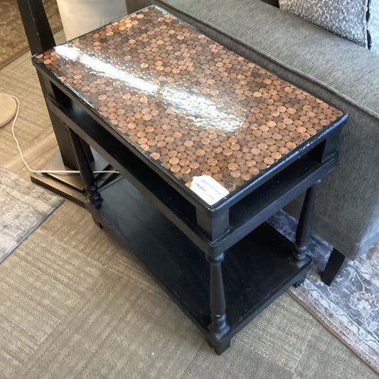 Small table with a decorative top made of pennies on a carpeted floor.
