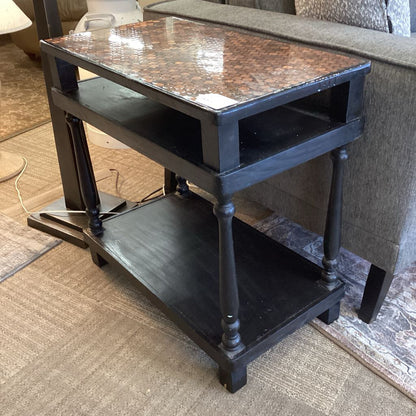Black metal side table with a textured top in a room setting.