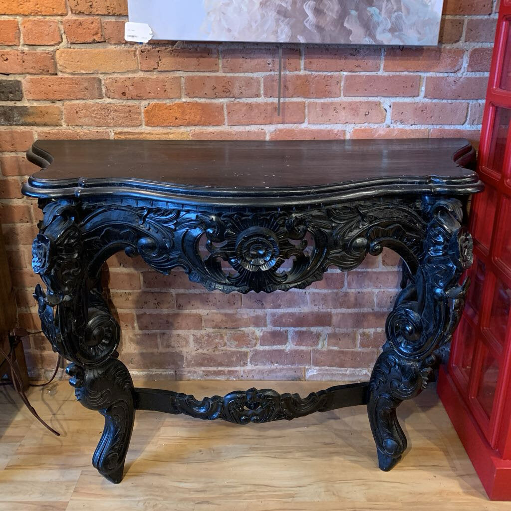 Decorative console table with intricate carvings against a brick wall.