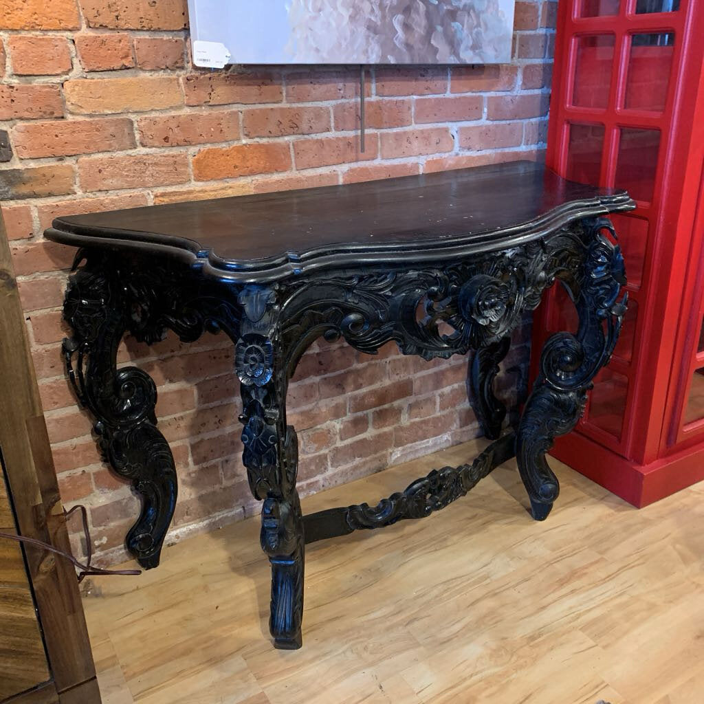 Decorative black console table against a brick wall with a red cabinet.