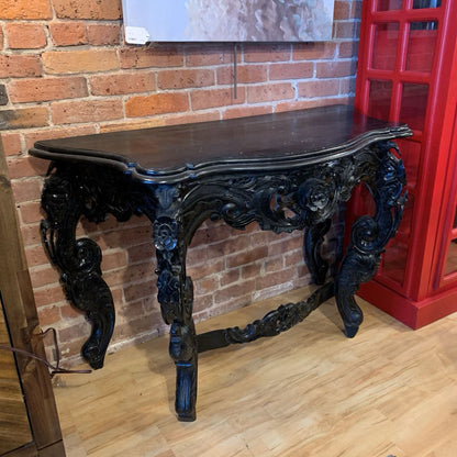 Decorative black console table against a brick wall with a red cabinet.