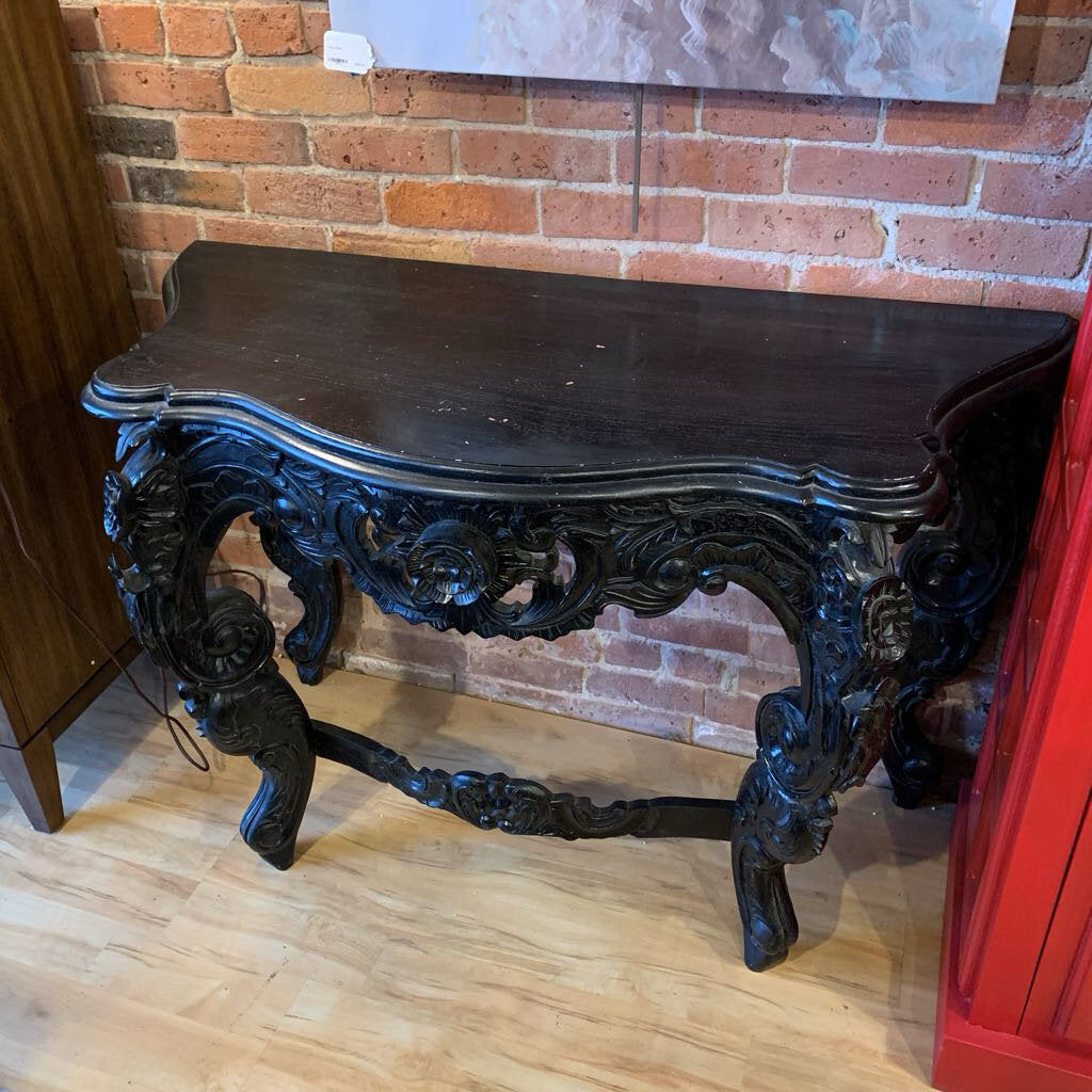Decorative black console table against a brick wall.