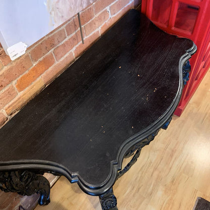 Black ornate table against a brick wall