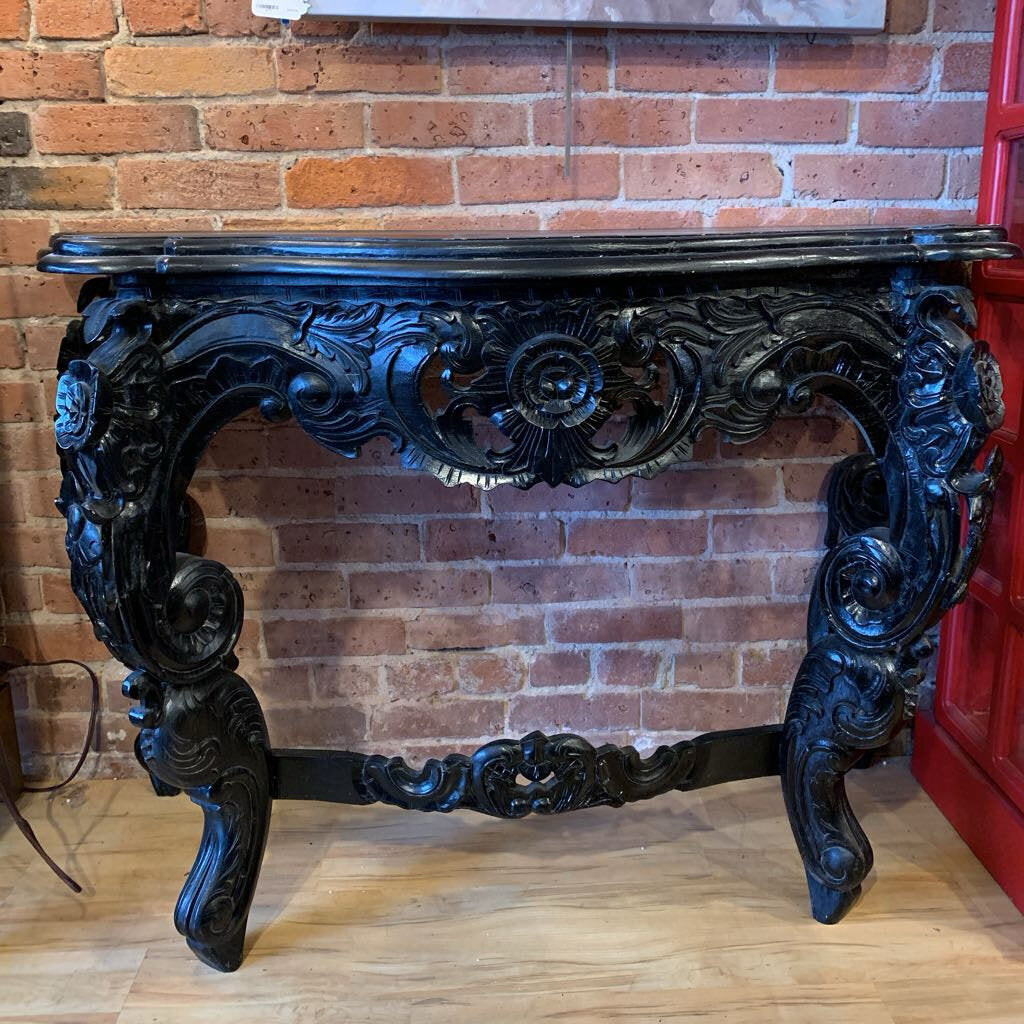 Decorative black console table against a brick wall.