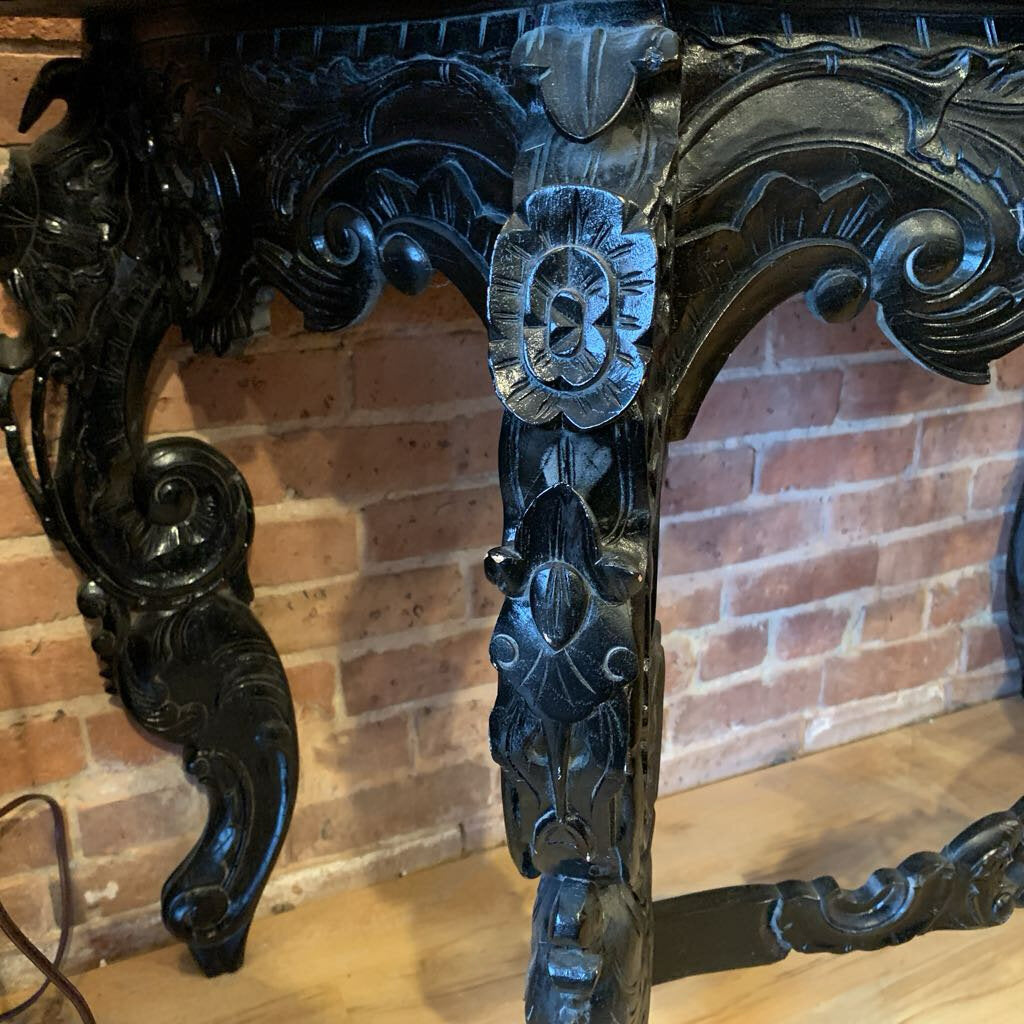 Decorative black metal chair with intricate designs against a brick wall.