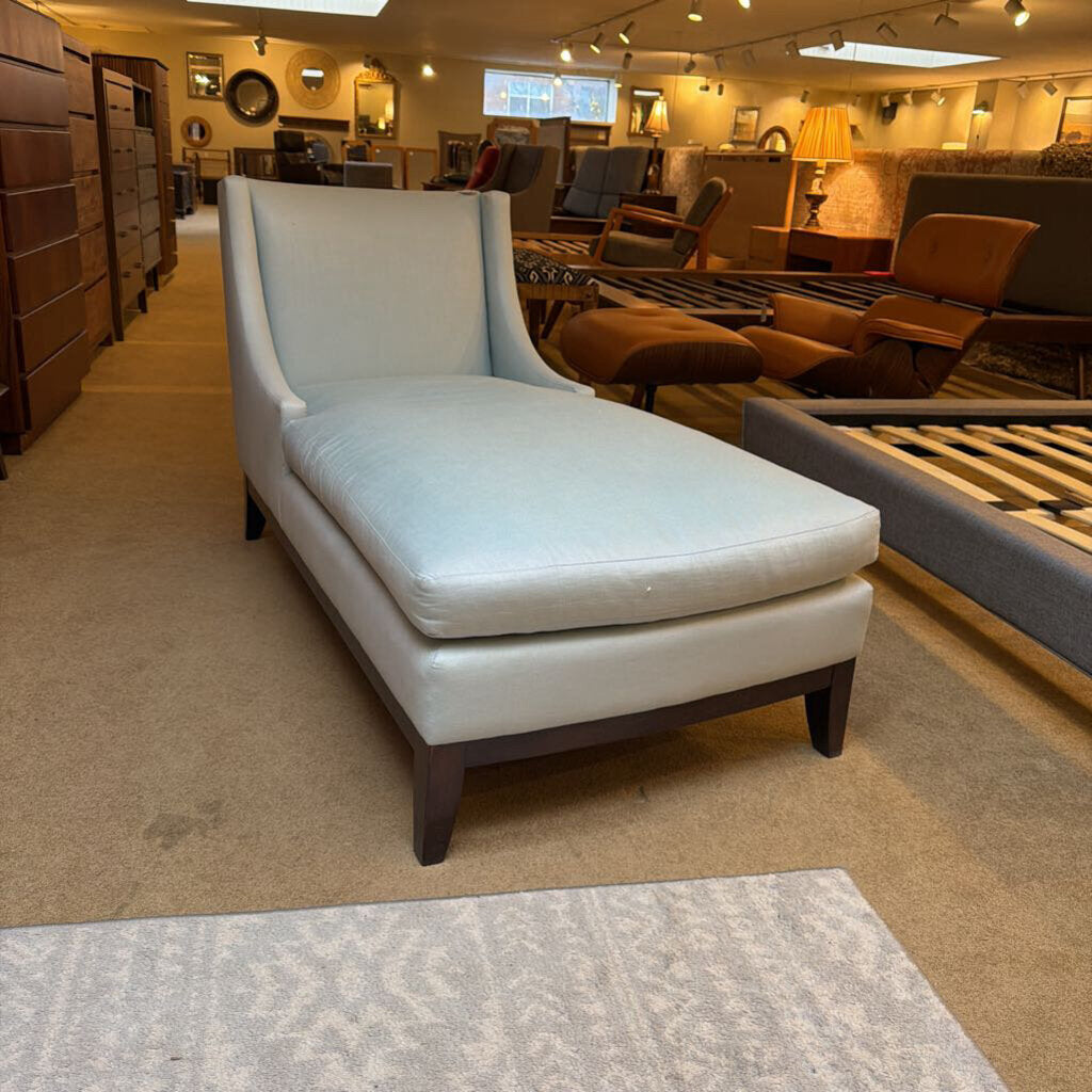 Light blue chaise lounge in a furniture store setting with various other furniture items.