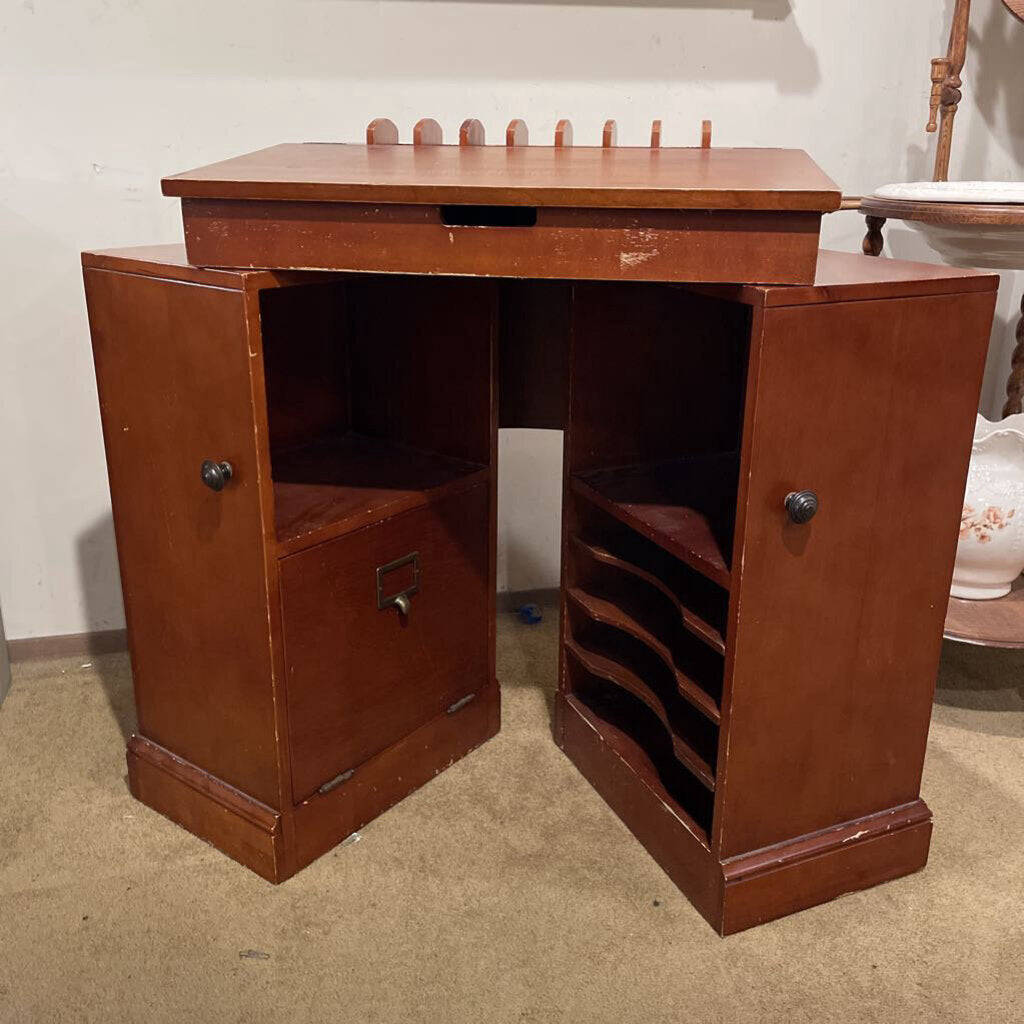 Wooden desk with open doors on a beige carpeted floor.