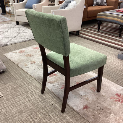Green upholstered chair in a showroom setting with furniture in the background
