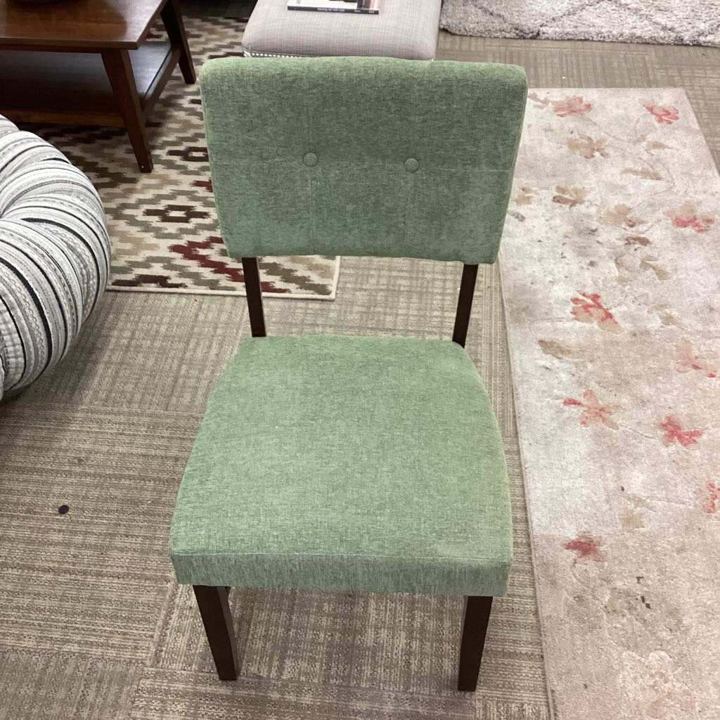 Green upholstered chair on a patterned rug with a striped ottoman in the background.