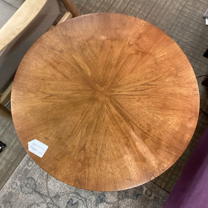 Round wooden table top with a visible brand label on a carpeted floor.