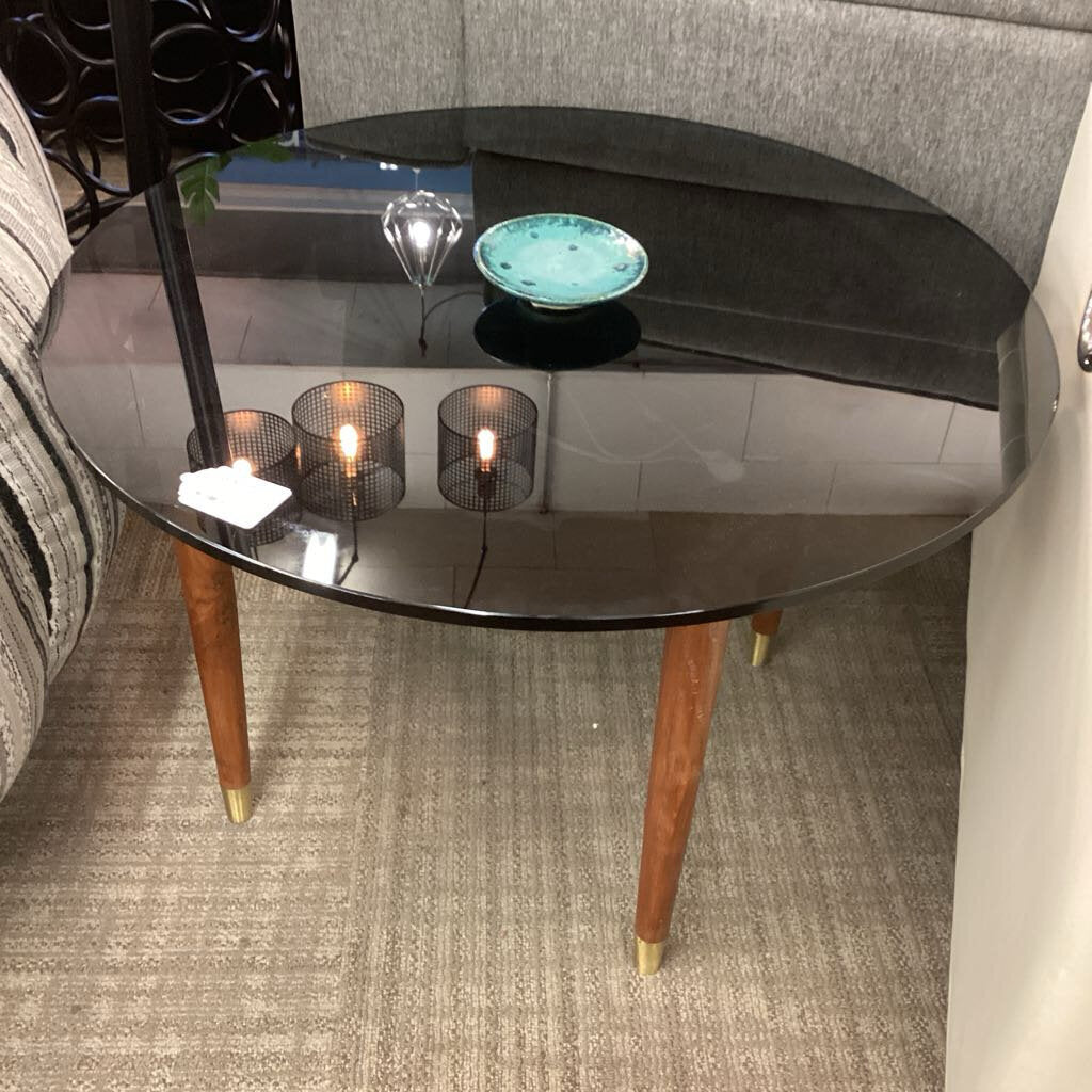 Round glass side table with wooden legs in a living room setting