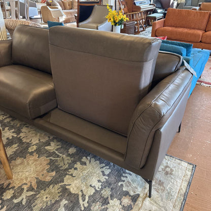 Brown leather sofa in a room with a patterned rug and other furniture.