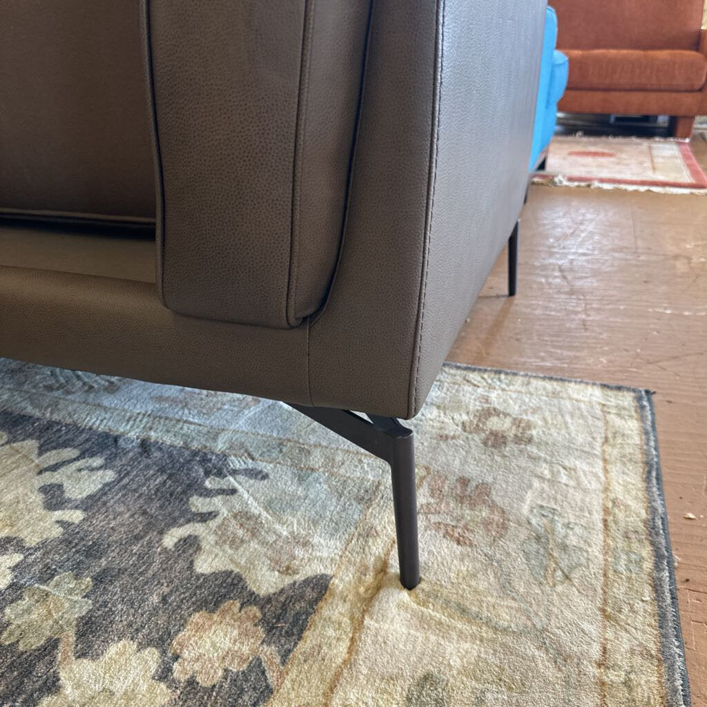 Brown leather sofa on a patterned rug with a wooden floor.