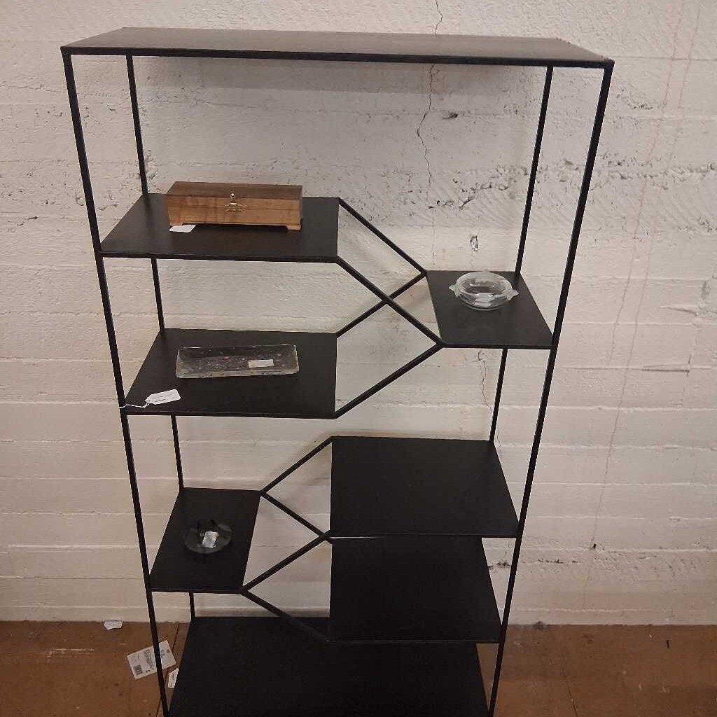 Black metal shelf with geometric design against a white brick wall.