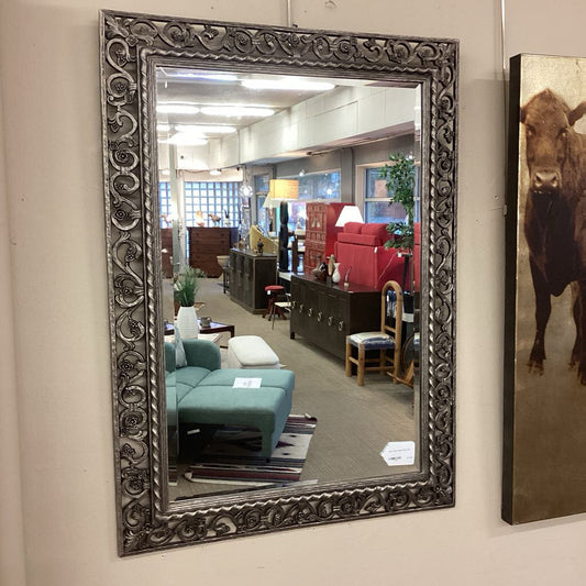 Decorative mirror with ornate frame on a wall, reflecting an interior setting.