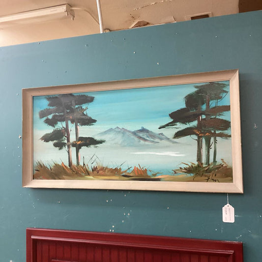 Framed landscape painting of trees and mountains on a teal wall.