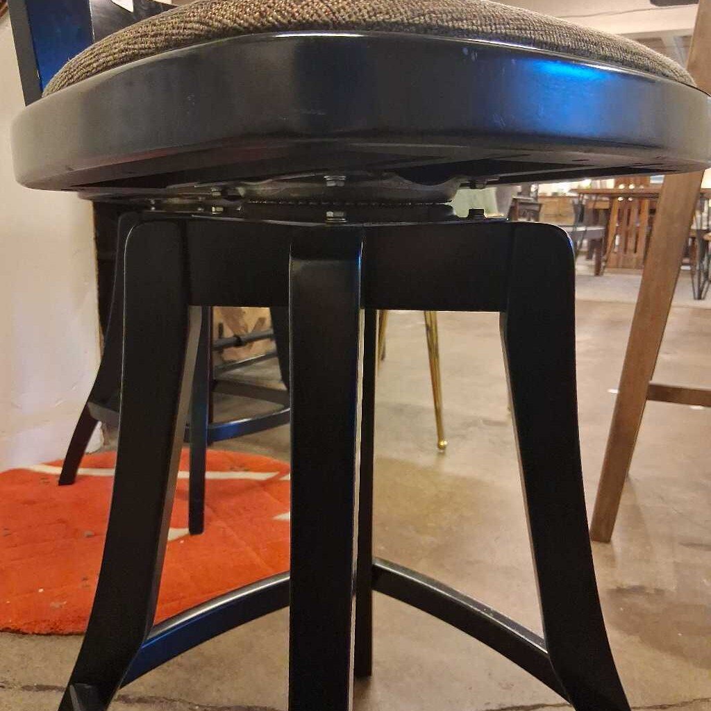 Bar stool with black metal legs and brown cushioned seat in a casual setting.