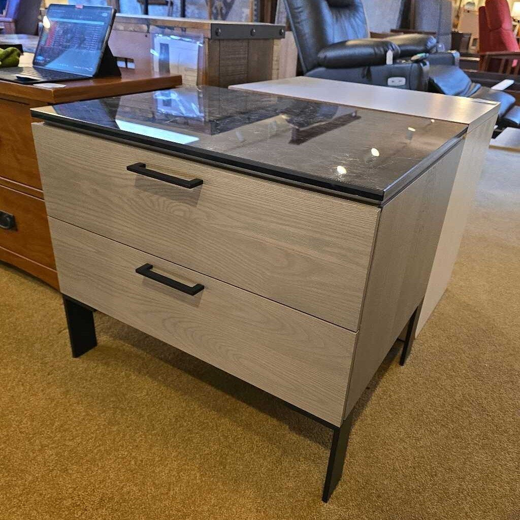 Two-drawer nightstand with black glass top in a showroom setting