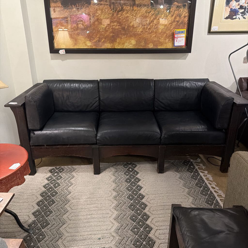 Black leather sofa in a room with a patterned rug and framed pictures on the wall.