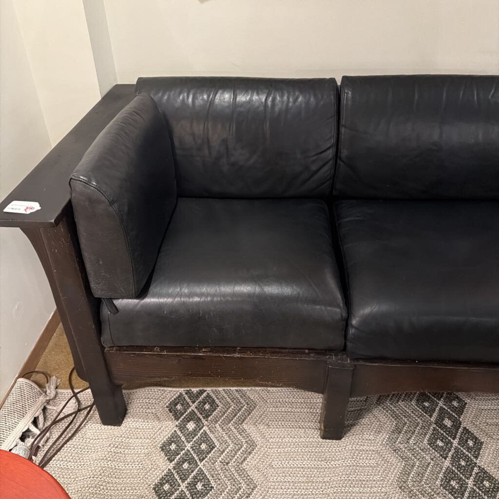 Black leather sectional sofa in a room with a patterned rug.