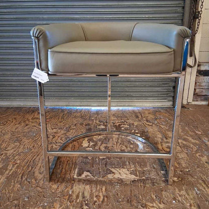 Bar stool with green cushioned seat and metal frame on a wooden floor.