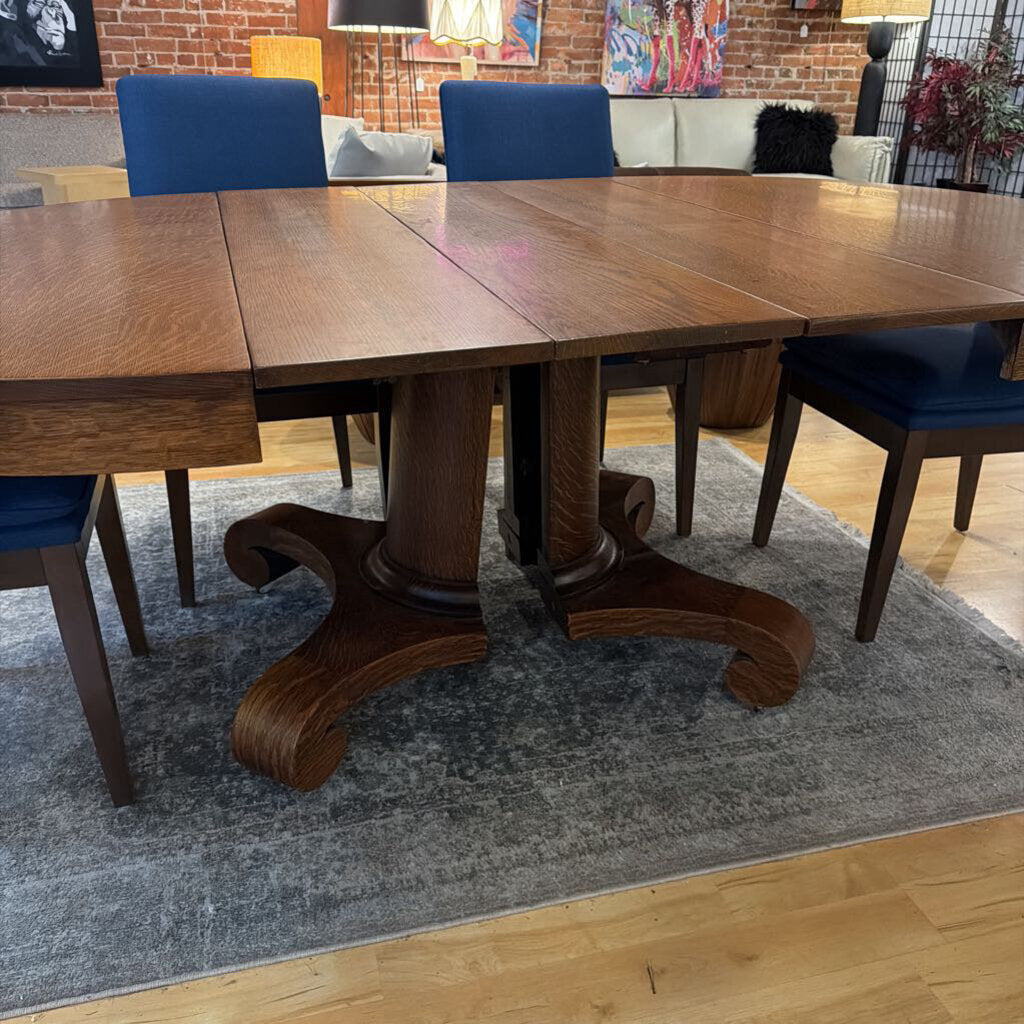 Wooden dining table with four blue chairs in a room with a brick wall and rug.