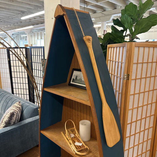 A-frame bookshelf with wooden paddle and decorative items in a room with plants and a couch.