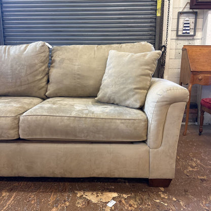 Beige sofa with visible wear in a room with a wooden floor and a metal shutter.