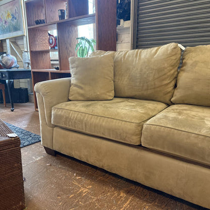 Beige sofa in a room with wooden floor and shelves.