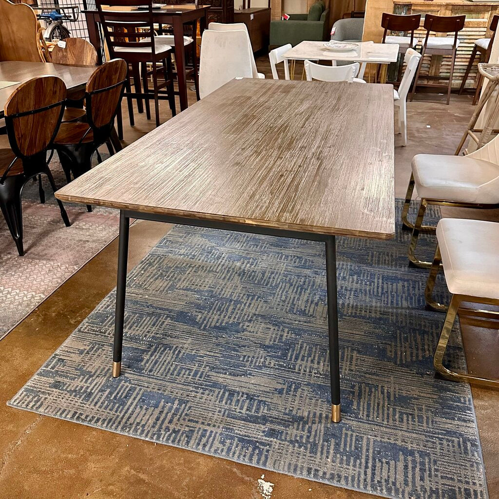 Wooden dining table with metal legs on a blue patterned rug in a showroom setting.