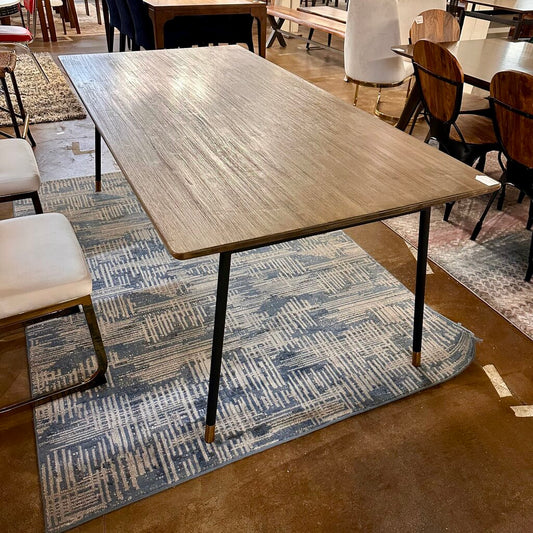 Dining table with wooden surface and metal legs on a patterned rug in a room with chairs and tables.