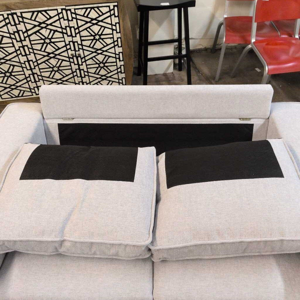 Gray sofa with black cushions in a room with red chairs and a geometric wall design.