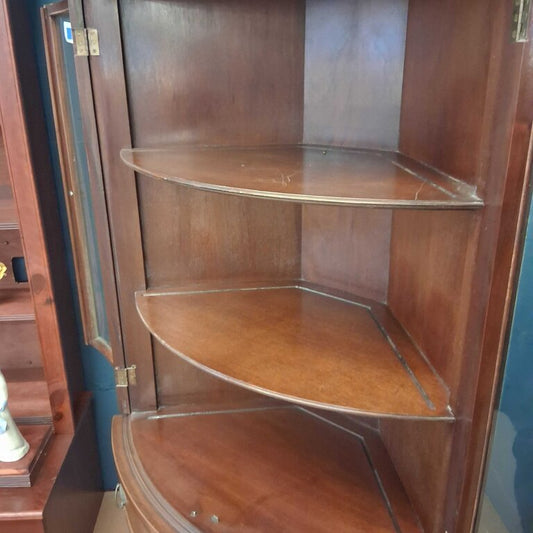 Wooden corner cabinet with glass shelves in a room setting.