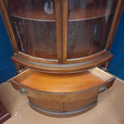 Wooden corner display cabinet with glass doors against a blue wall.
