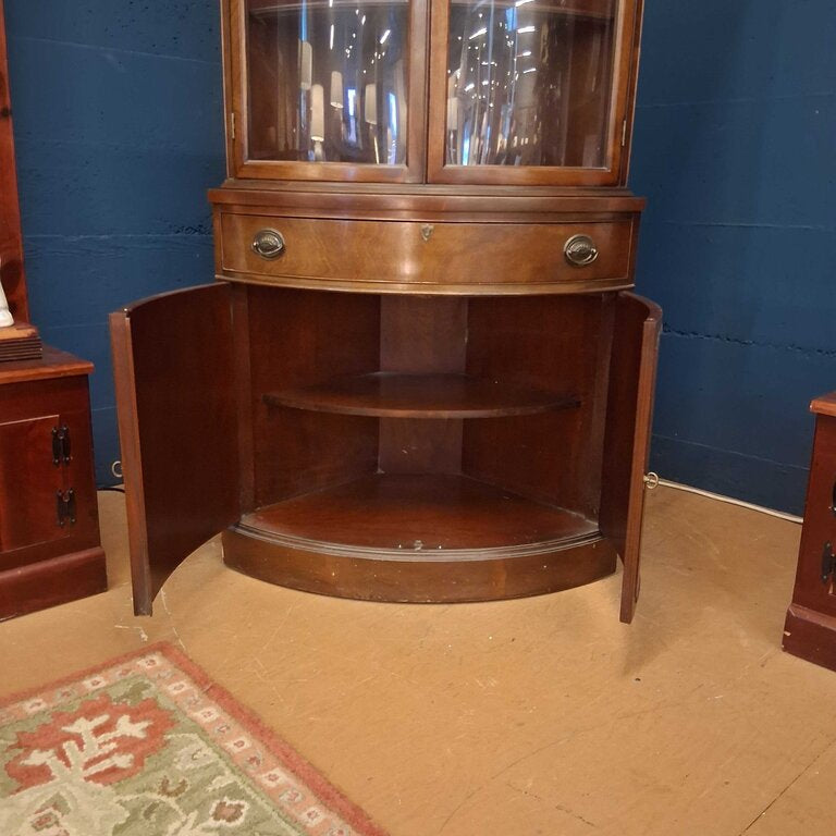 Wooden corner cabinet with glass doors against a blue wall.