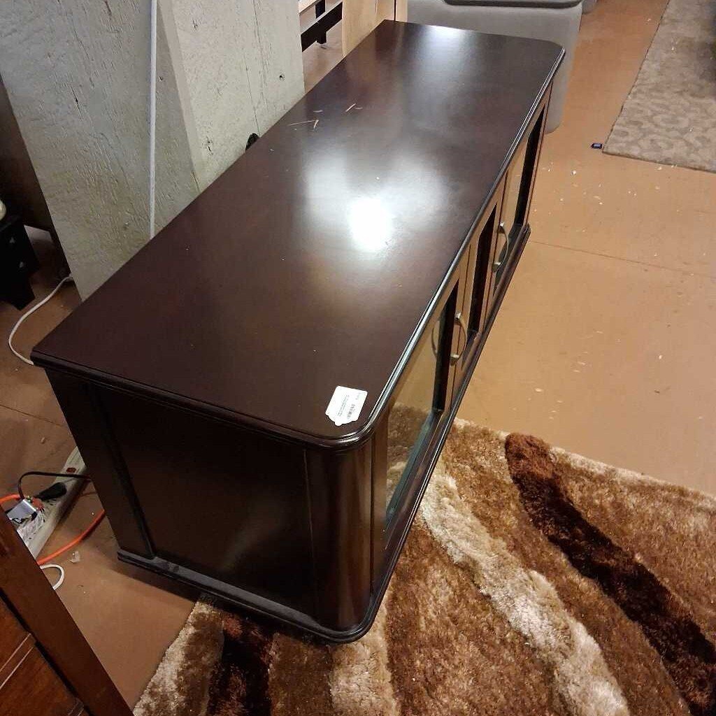 Dark brown wooden desk on a carpeted floor with a neutral wall in the background