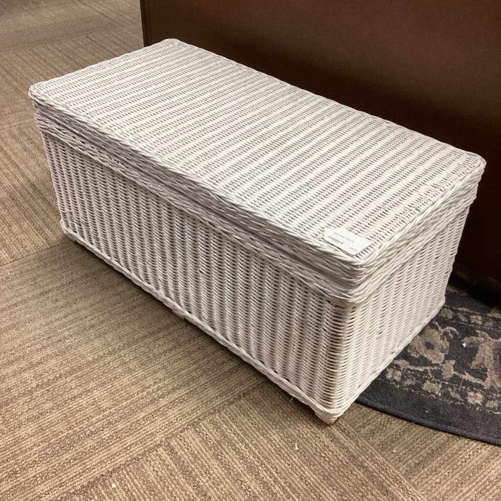 White woven ottoman with striped cushion on a carpeted floor.