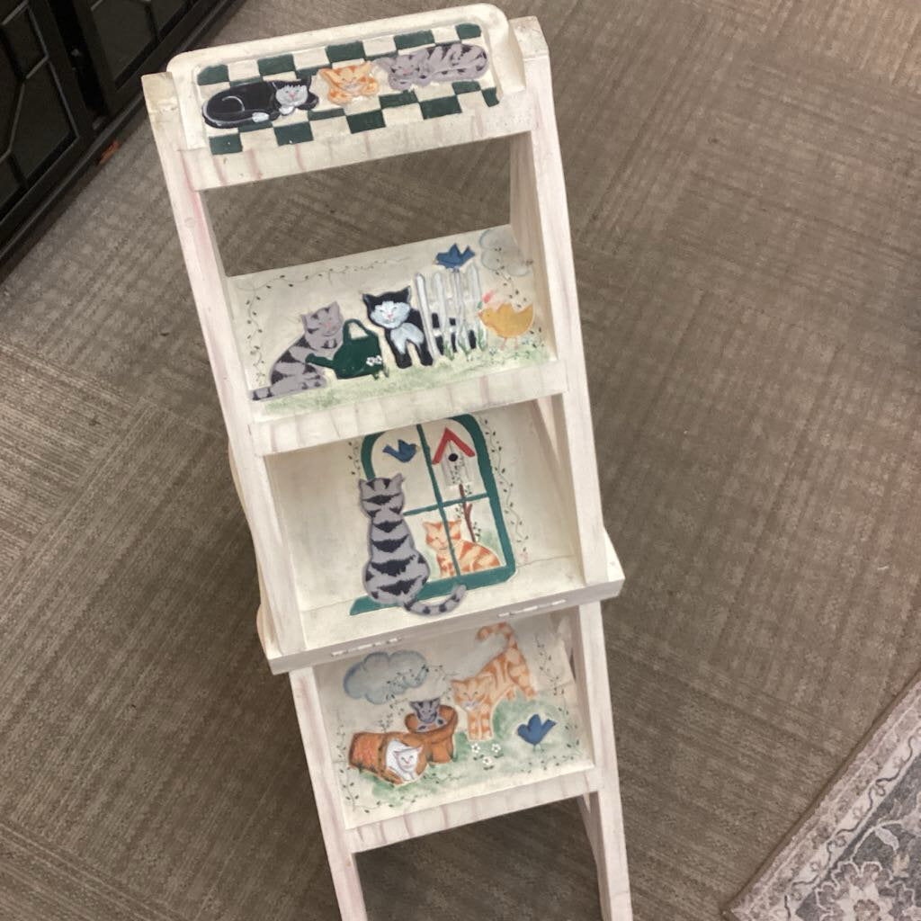 White three-tiered shelf with cat-themed decorations on a carpeted floor.