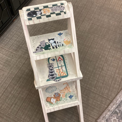 White three-tiered shelf with cat-themed decorations on a carpeted floor.