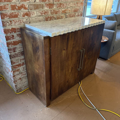 Wooden cabinet with a stone countertop against a brick wall in a room with a couch and lamp.