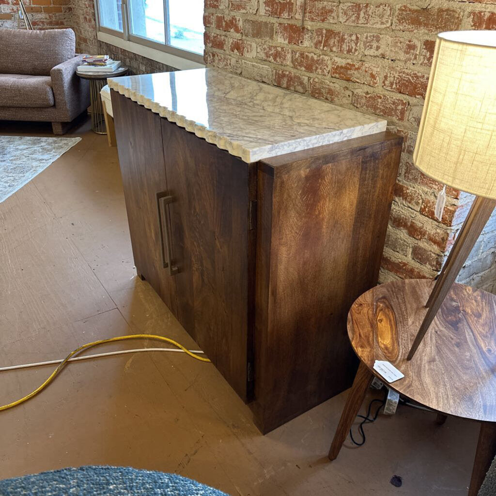 Wooden bar counter with marble top in a room with brick wall and furniture.